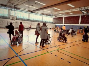 Kinder im Rollstuhl und Erwachsene in der Sporthalle