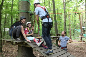 Drei lachende Personen auf einer Seilrutsche im Kletterwald.