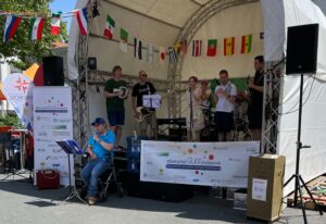 Eine inklusive Band spielt auf einer Bühne mit internationalen Flaggen im Hintergrund bei einer Veranstaltung von oberursel all inclusive