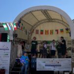 Eine inklusive Band auf einer Bühne bei einem Bandmeeting in Oberursel, umgeben von internationalen Flaggen und Bannern mit dem Schriftzug 'Oberursel All Inclusive'