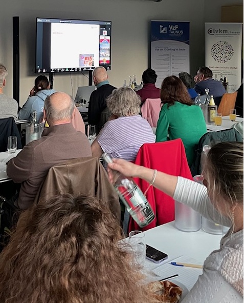 Mehrere Personen sitzen in einem Seminarraum und schauen auf einen Bildschirm mit Präsentation