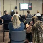 Mehrere Personen sitzen in einem Seminarraum und schauen auf die Präsentation auf einem Monitor