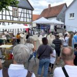Mehrere Menschen stehen und sitzen vor einer kleinen Bühne im Freien, auf der eine inklusive Musikgruppe auftritt.