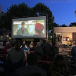 Blick auf die Leinwand in der Dämmerung. Davor die Zuschauer und rechts neben der Leinwand die Gebärdensprachdoltscherinnen