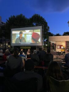 Blick auf die Leinwand in der Dämmerung. Davor die Zuschauer und rechts neben der Leinwand die Gebärdensprachdoltscherinnen
