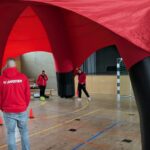 Drei Personen spielen in der Sporthalle vor einem Tor Fußball
